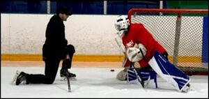 A hockey goalie in red gear blocks a shot from a player on ice.